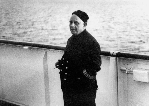 Νεαρός Νίκος Καββαδίας με ναυτικό κασκέτο και τσιγάρο στο στόμα, με τα χέρια στη μέση, πάνω σε πλοίο
