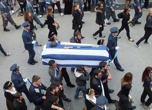 Συγγενείς και φίλοι μεταφέρουν στον δρόμο το φέρετρο της Άννας Πολλάτου, καλυμμένο με ελληνική σημαία, με στρατιωτικούς δίπλα
