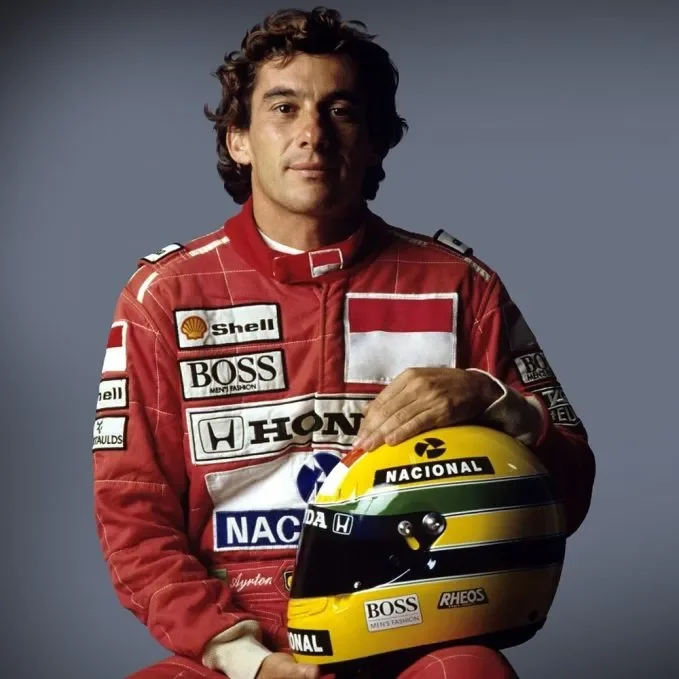 Πορτρέτο του Βραζιλιάνου οδηγού της Formula 1, Άιρτον Σένα, ο οποίος φοράει την κόκκινη αγωνιστική φόρμα της McLaren και κρατάει το χαρακτηριστικό κίτρινο, πράσινο και μπλε κράνος του στα χέρια του.