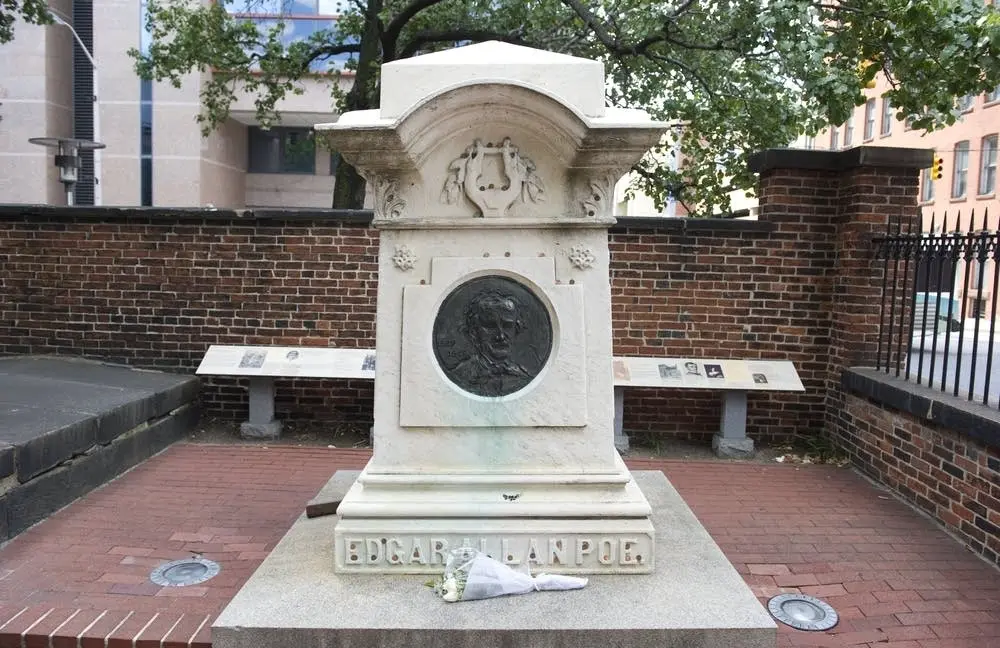 Το μαρμάρινο μνημείο του Edgar Allan Poe στη Βαλτιμόρη, με ανάγλυφο μετάλλιο προσωπογραφίας, σκαλισμένη λύρα στην κορυφή, την επιγραφή «EDGAR ALLAN POE» στη βάση και ένα μικρό μπουκέτο λουλούδια μπροστά
