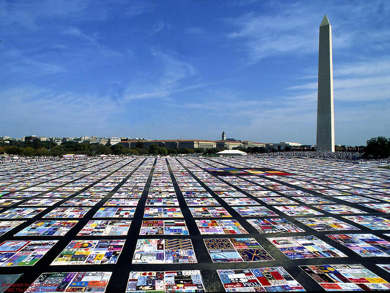 Πανοραμική φωτογραφία του AIDS Memorial Quilt απλωμένου στο έδαφος σε πολλές σειρές, με το Washington Monument και μπλε ουρανό στο βάθος