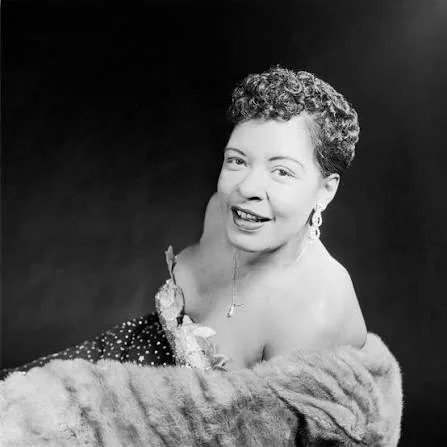 Ασπρόμαυρο πορτρέτο της Billie Holiday με σγουρά κοντά μαλλιά, σκουλαρίκια και γούνινο σάλι