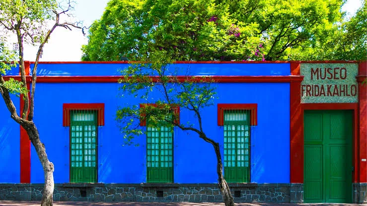 Η μπλε πρόσοψη της Casa Azul με κόκκινα πλαίσια, πράσινα παράθυρα και την επιγραφή «Museo Frida Kahlo»