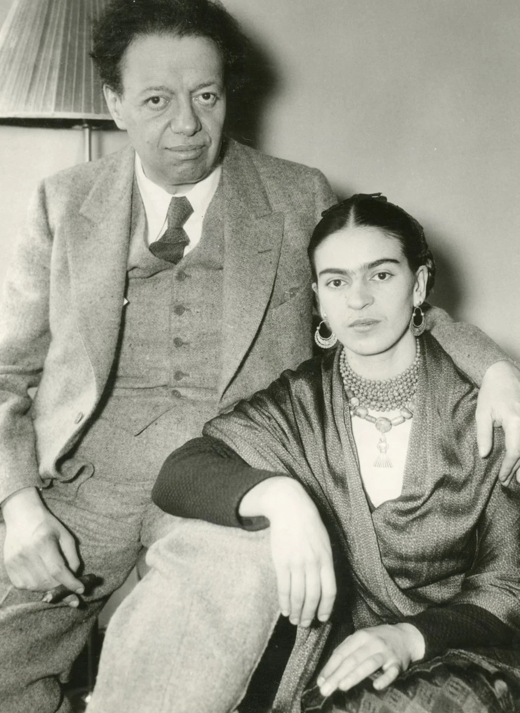 Ασπρόμαυρη φωτογραφία του Diego Rivera και της Frida Kahlo, καθισμένων δίπλα-δίπλα· εκείνος έχει το χέρι γύρω της και κρατά πούρο