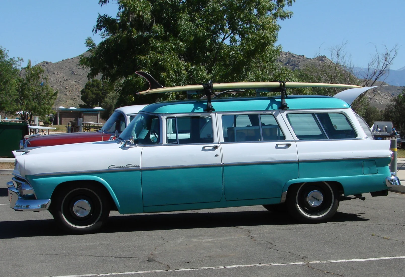 Τιρκουάζ και λευκό Ford station wagon της δεκαετίας του 1950 με σανίδα του σερφ στην οροφή, σε χώρο στάθμευσης