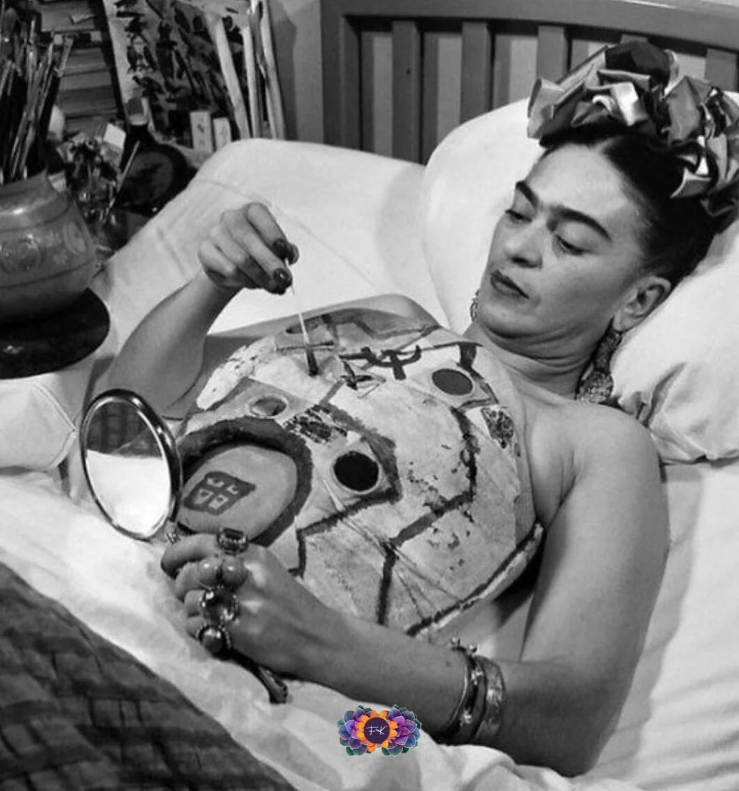 Ασπρόμαυρη φωτογραφία της Frida Kahlo ξαπλωμένης στο κρεβάτι, που ζωγραφίζει με πινέλο ένα κορσέ με σχέδια, με έναν καθρέφτη στο χέρι