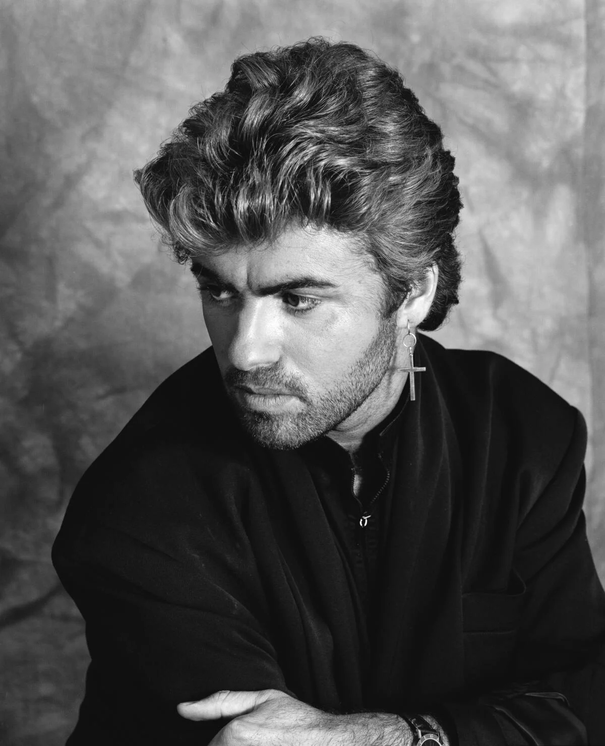 Ασπρόμαυρο πορτρέτο του George Michael με σκούρο σακάκι και σκουλαρίκι σε σχήμα σταυρού.