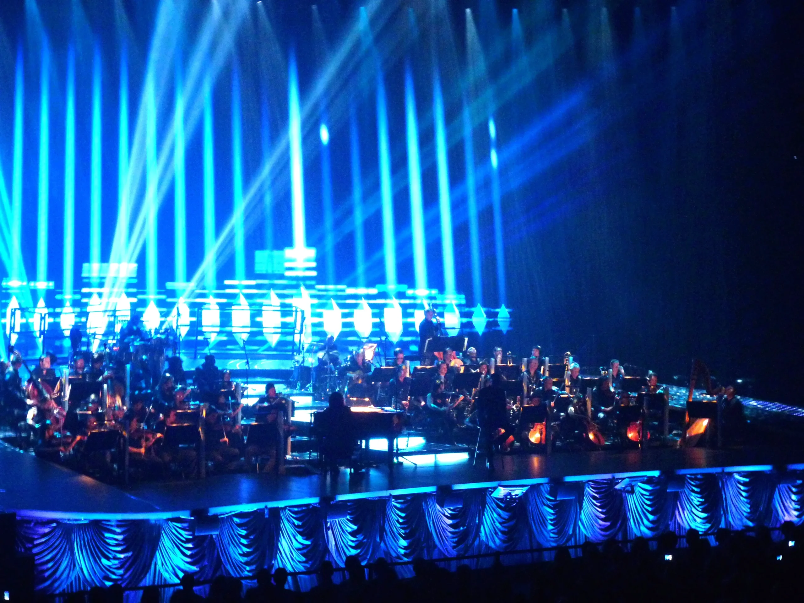 Η ορχήστρα της Symphonica στη σκηνή του Palais Nikaia με μπλε φωτισμό.
