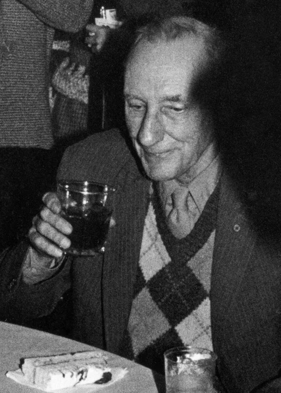 Ο William S. Burroughs καθισμένος σε τραπέζι, κρατώντας ποτήρι