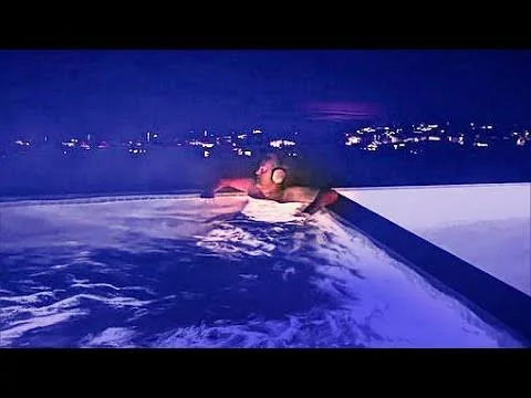 Στιγμιότυπο βίντεο με άτομο που ακουμπά στην άκρη της πισίνας τη νύχτα, με φώτα της πόλης στο βάθος