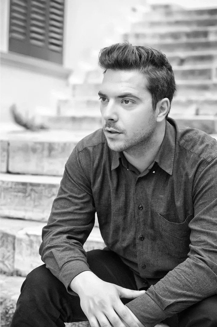 Ο Πάνος Νάτσης καθιστός σε σκάλες, σε ασπρόμαυρη φωτογραφία