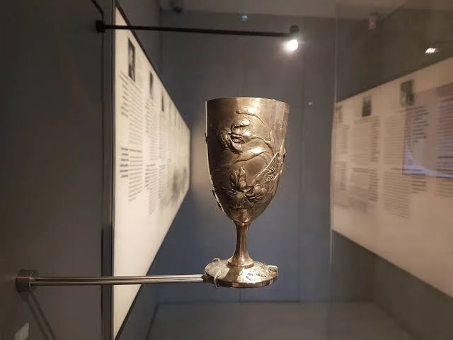 Το ασημένιο κύπελλο με ανάγλυφο διάκοσμο και ελληνική επιγραφή σε εκθεσιακή προθήκη.