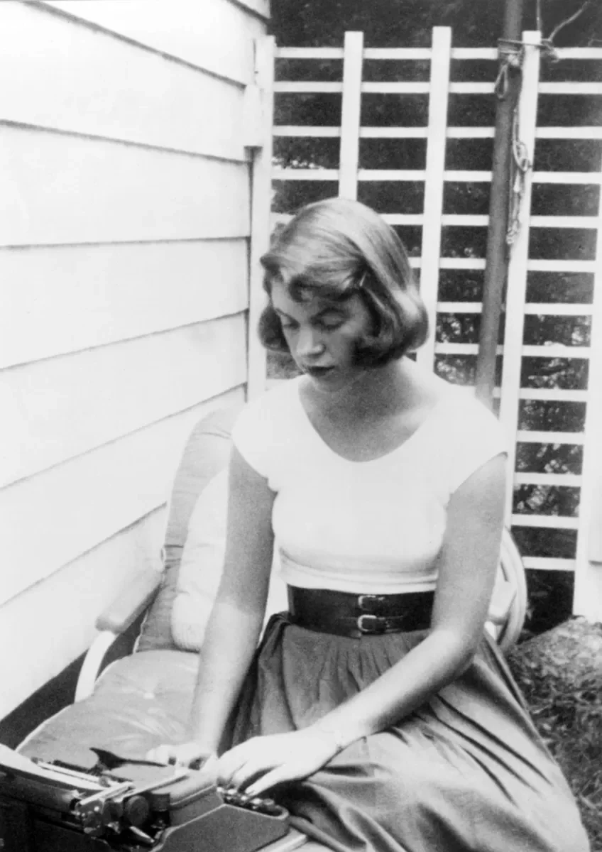 Η Sylvia Plath κάθεται σε εξωτερικό χώρο και πληκτρολογεί σε γραφομηχανή.