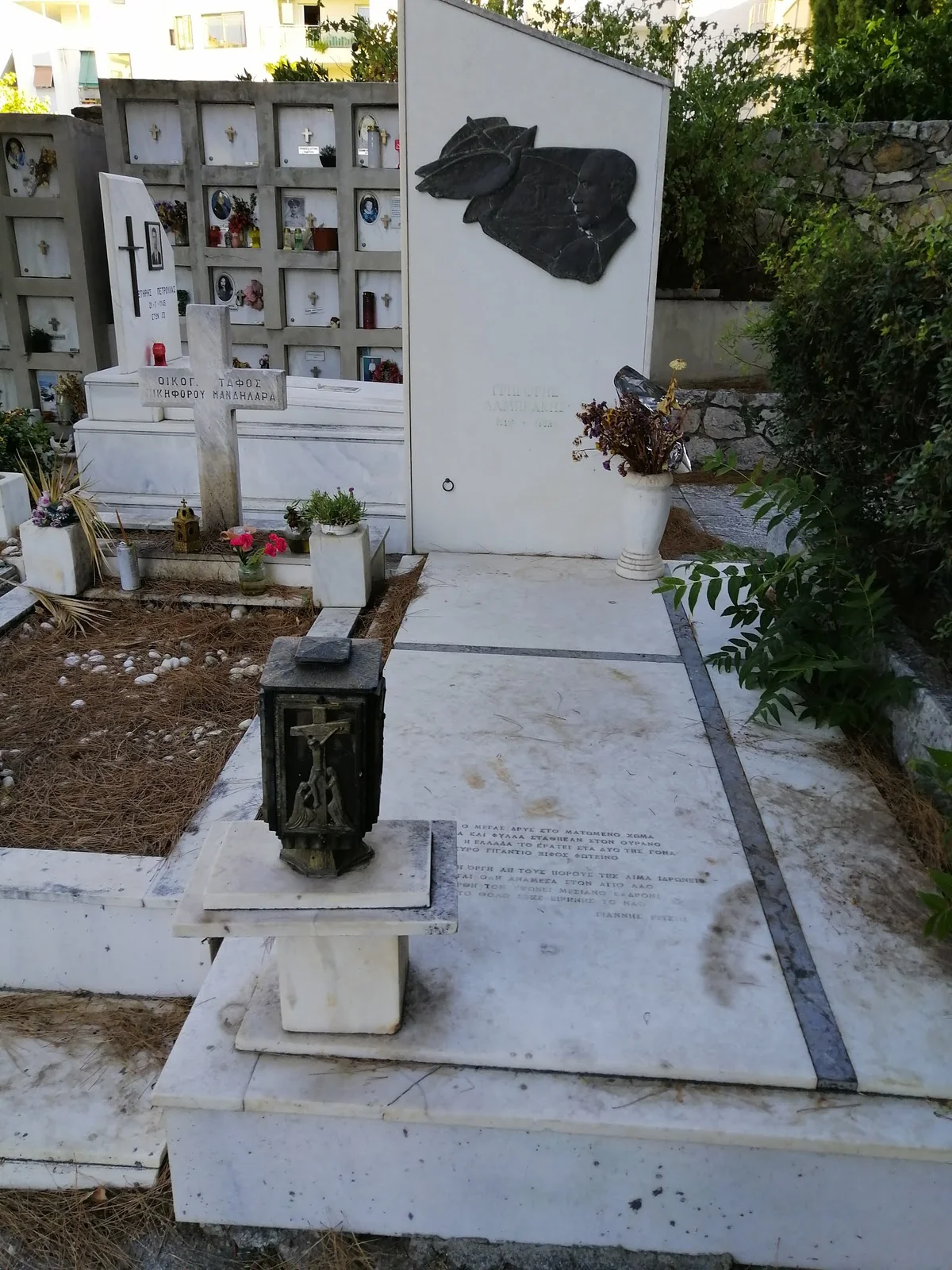 Ο τάφος του Γρηγόρη Λαμπράκη, με λευκή μαρμάρινη στήλη, ανάγλυφο πορτρέτο και στίχους του Γιάννη Ρίτσου στην πλάκα