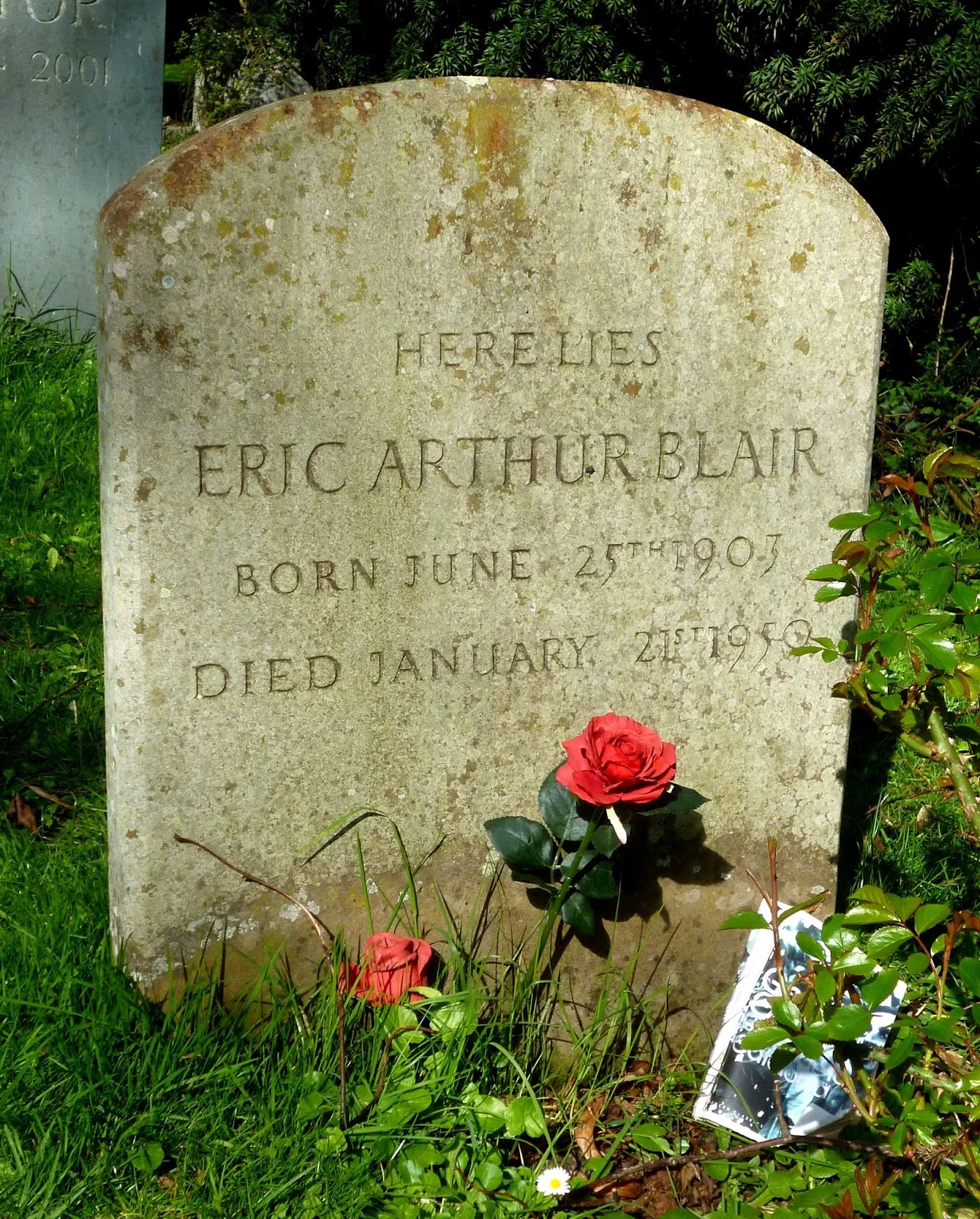 Πέτρινη ταφόπλακα με την επιγραφή «Here lies Eric Arthur Blair, born June 25th 1903, died January 21st 1950», με τεχνητά κόκκινα τριαντάφυλλα μπροστά της