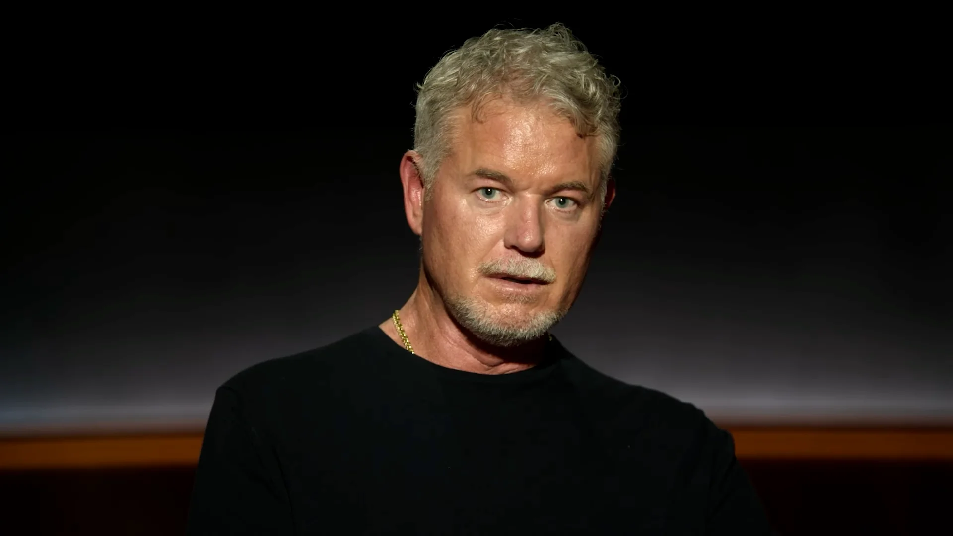 Κοντινό πορτρέτο του Eric Dane με σοβαρή έκφραση, σε σκούρο φόντο