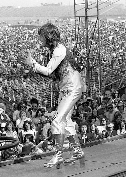 Ο νεαρός Ozzy Osbourne στη σκηνή μεγάλου φεστιβάλ τη δεκαετία του 1970, με λευκό πουκάμισο με κρόσσια και μπότες πλατφόρμες