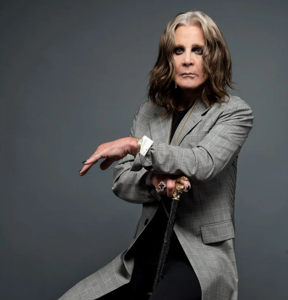 Ο ηλικιωμένος Ozzy Osbourne με γκρίζα μαλλιά και καρό σακάκι, να στηρίζεται σε μαύρο μπαστούνι